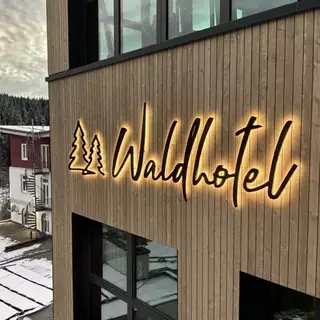 Logo und 3D-Buchstaben LED-Rückbeleuchtung, auf einer Außenwand aus Holzlamellen angebracht.