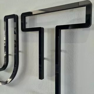 3D-Buchstaben aus schwarz poliertem Edelstahl auf Hartschaum, mit Distanzhaltern montiert.