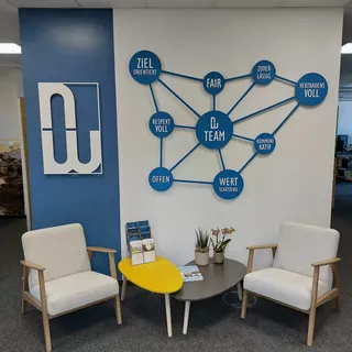 Sitzbereich mit einer weißen Wand im Hintergrund, auf der ein Acrylglas-Design in Form einer chemischen Formel montiert ist.