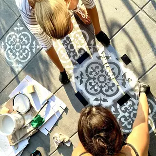 Zwei Frauen richten eine Schablone auf dem Boden aus und fixieren sie 