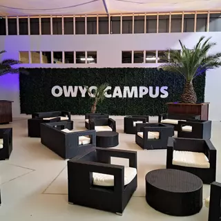 Eingangsbereich mit Sitzgelegenheiten und einem Tresen im Hintergrund, an dem weiße Acrylglasbuchstaben montiert sind.