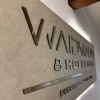 3D-Buchstaben aus Verbundmaterial in Hairline Gold, selbstklebend auf einer hellen Wand angebracht und aus seitlicher Perspektive aufgenommen.