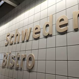 Das Logo ist aus hochwertigem Holz gefertigt und sorgfältig an der Wand angebracht. Es zeigt ein kreatives, maßgeschneidertes Design, das durch seine natürliche Holzmaserung und präzise Verarbeitung hervorsticht. Das Logo fügt sich harmonisch in die Umgebung ein und verleiht dem Raum eine warme, einladende Atmosphäre