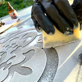 Eine Kunststoffschablone liegt auf Steinen, es wird Farbe mit einem Schwamm aufgetupft