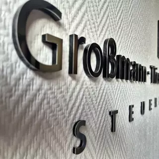 3D-Buchstaben und Logo aus silber Edelstahl auf Acrylglas, selbstklebend montiert.