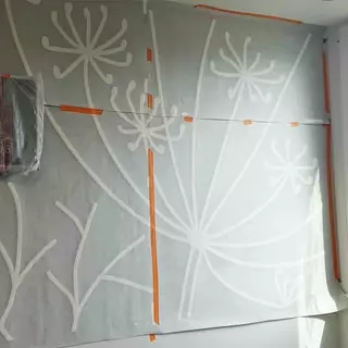 An XXL wall stencil is being applied, featuring a floral design