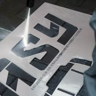 Eine Metallschablone wird mit einem Wasserhochdruckreiniger verwendet, um ein reverse Graffiti auf einen Bürgersteig zu sprühen 
