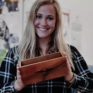 A woman presents her wooden box with a company branding.